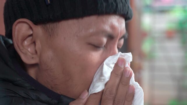 Asian man, cleaning his nose and house for respiratory influenza, allergies and sinus disease or infection. Viral disease and toilet paper to remove bacteria in the living room, fatigue and tissue for