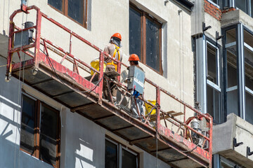 August 21, 2025: Construction lift with workers performing wall finishing on a building site in...
