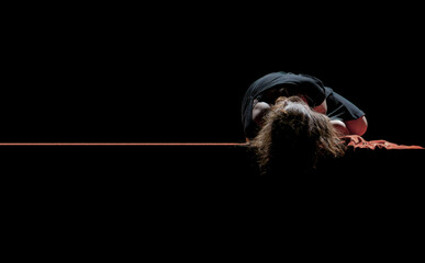 A solitary figure lies curled on a dark surface, illuminated by a theatrical spotlight. The composition evokes vulnerability, introspection, and emotional depth—perfect for editorial covers in drama