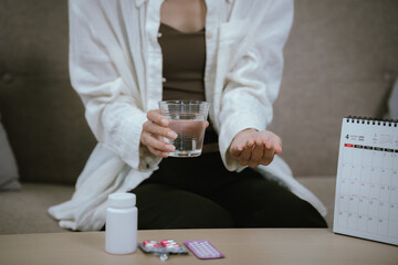 Close-up of a woman holding a glass of water and pills beside a calendar, representing medication...