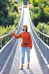 Travel and photography. A young woman with a camera and a backpack walks along a suspension bridge. Happy female tourist traveler enjoying her trip.