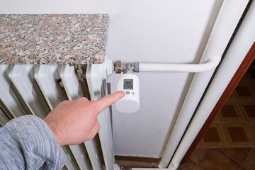 Close-up of hand lowering smart radiator thermostat. Concept of responsible energy saving, reducing...