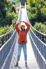young woman with a camera and a backpack enjoys a walk along the suspension bridge. Happy female tourist enjoying her trip.