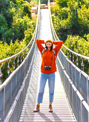 young woman with a camera and a backpack enjoys a walk along the suspension bridge. Happy female tourist enjoying her trip.