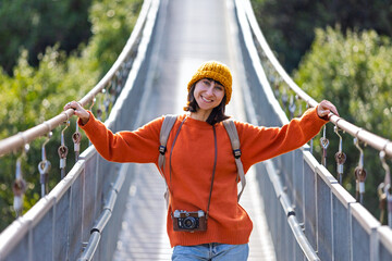 Travel and photography. A young woman with a camera and a backpack walks along a suspension bridge. Happy female tourist traveler enjoying her trip and taking photos.
