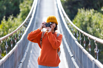 Travel and photography. A young woman with a camera and a backpack walks along a suspension bridge. Happy female tourist traveler enjoying her trip and taking photos.