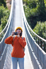Travel and photography. A young woman with a camera and a backpack walks along a suspension bridge. Happy female tourist traveler enjoying her trip and taking photos.