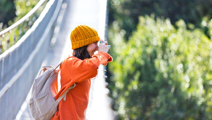 stylish young woman in a hat and with a backpack takes pictures with the camera in sunny weather. Travel and photography. Happy female tourist enjoying her trip.