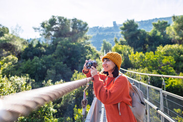 Travel and photography. A young woman with a camera and a backpack enjoys the view from the suspension bridge. Happy female tourist enjoying her trip.