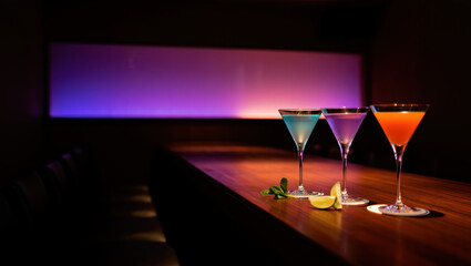 Few colorful cocktails line a gleaming marble bar in a cozy lounge&mdash;green, pink, blue, amber, and berry‑red drinks with citrus, mint, and pineapple garnishes under warm, moody lights.