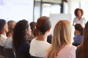 Close up of a Group of female executives attend corporate event. Audience watches facing projection screen with female ceo presenting business performance presentation . 