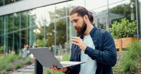 Successful bearded businessman greeting colleagues with hand gesture during online conference on...