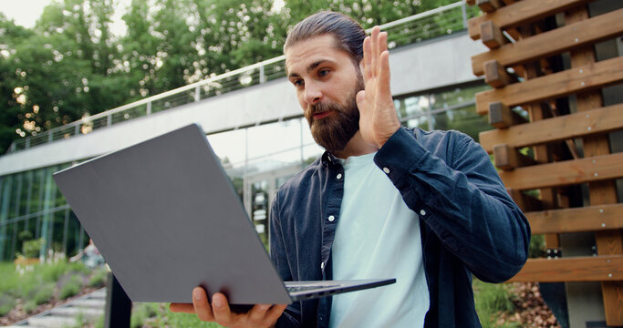 Bearded businessman taking part in an online business meeting on a laptop outdoors, remote work and digital communication concept - Powered by Adobe