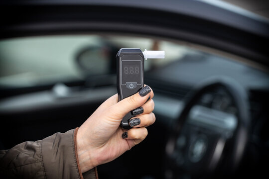 Hand With Manicure Holds Breathalyzer Inside Vehicle. Close-Up Of Sobriety Checking Device.