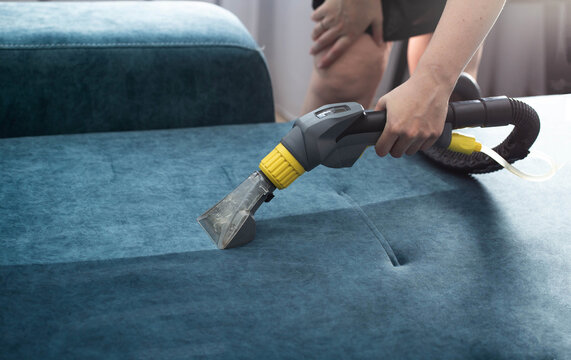 Cleaning a blue fabric couch using a professional upholstery cleaning machine in a bright living room