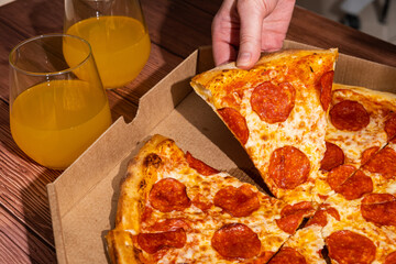 Delicious pepperoni pizza being served from a takeout box, accompanied by refreshing orange drinks in glasses, creating a vibrant and inviting dining experience