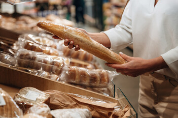 Individual is selecting a fresh baguette from a bakery display, surrounded by various types of bread, showcasing the art of bread selection and appreciation