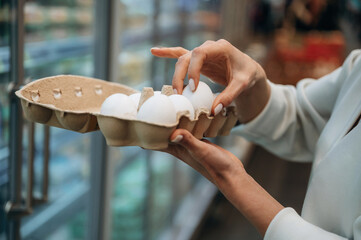 Obraz premium Woman selecting fresh eggs from carton in grocery store, showcasing careful choice and quality, emphasizing healthy food options and shopping experience