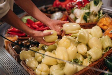 Woman selecting fresh yellow bell peppers from a vibrant display of vegetables in a market, showcasing healthy eating and organic produce choices