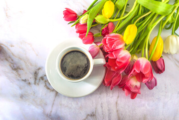 Valentine's day concept; top view for white cup of coffee and bunch of pink, yellow, white tulips on a marble background