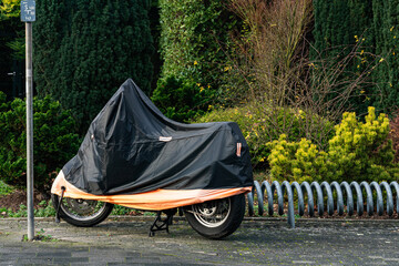 Motorcycle covered with a black and orange cover in a city