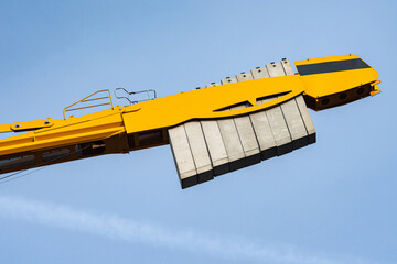 A yellow crane is lifting heavy concrete blocks under a clear blue sky