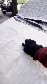 Mano escribiendo con nieve tras nevada en cristal de coche