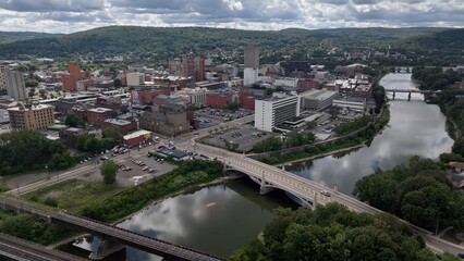 Binghamton city in New York State skyline with downtown buildings and business activity beside river in summer sunlight  