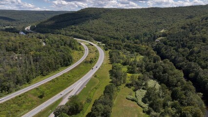 Driving across American countryside in the Catshill Mountains in New York State past green mountains and trees under blue sky and white clouds in summer on road trip family vacation