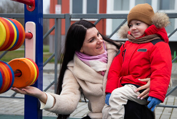 Woman and young boy playing outdoors, engaging with colorful abacus toy. Parent and child happiness and bond during cool weather activity. Mother holding son with care.