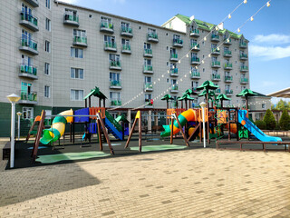 Vibrant outdoor playground with slides, swings, and climbing structures, inviting children to play, set against a modern residential complex with many balconies under a bright blue sky.