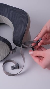 Hands demonstrate the process of attaching a strap to a travel neck pillow, showcasing the connection of the strap to the pillow's clip for secure use and comfort
