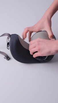 Hands demonstrate the process of folding a flexible travel pillow into a compact shape, showcasing the transformation from a curved form to a rolled-up design for easy storage