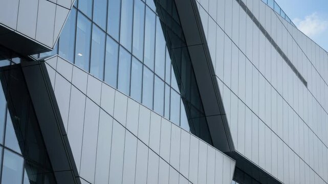 modern glass and metal office building facade with angular geometric panels and reflective windows under clear daytime sky