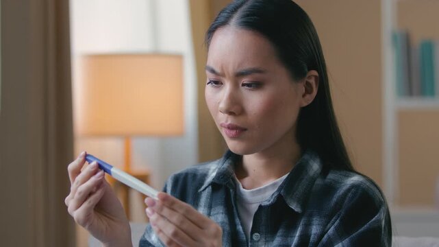Shocked pregnant Asian Korean young woman holding positive pregnancy test at home worried female surprised anxious stressed girl unplanned pregnancy reaction unwanted child baby fertility motherhood