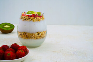 Delicious layered yogurt parfait glass featuring wholesome rolled oats, fresh strawberries, and vibrant kiwi fruit slices offers a healthy breakfast