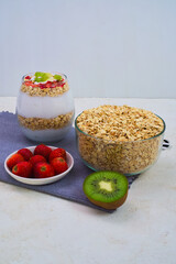Layered yogurt parfait with fresh strawberries, kiwi pieces, and a generous bowl of raw rolled oats ready for a healthy breakfast preparation.