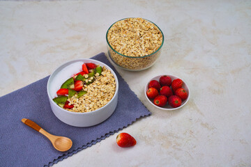 Healthy bowl of overnight oats topped with fresh sliced kiwi and strawberries alongside a jar of rolled oats and berries for breakfast preparation.