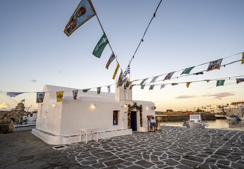 White Cycladic Greek Orthodox Church of Agios Nikolaos at sunset, decorated with flags, harbour of Naoussa, Naoussa, Paros, Cyclades, Greece
