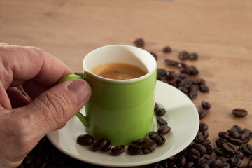 Hand holding green espresso cup with coffee beans on table