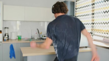 A man in a printed T-shirt and headphones spins in the kitchen leaning