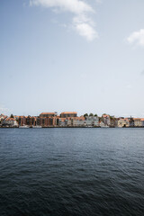 panoramic view of a picturesque waterfront town with colorful historic buildings lining the shore, reflected in calm water beneath a clear, open sky. Denmark