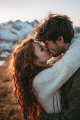 Romantic couple sharing intimate kiss in cozy sweaters at mountain sunset.