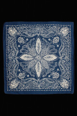 Top-down view of a classic blue bandana with intricate white floral and paisley designs, neatly spread out against a solid black background.