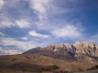 Majestic mountain range under a bright blue sky with fluffy clouds, showcasing rugged terrain and natural beauty, inviting exploration and adventure in the great outdoors