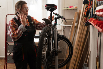 Woman mechanic repairing Bicycle in garage using phone in small business. service, maintenance and tools for bike