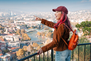 Woman backpacking, pointing at a panorama of the old city of Tbilisi, Georgia, with a river and bridge © EdNurg