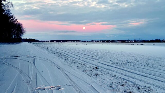 Winter landscape of snow covered field and road with pastel moonset above horizon