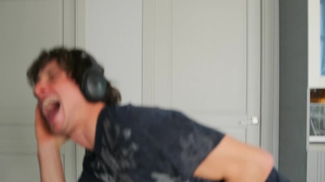 An energetic man in a black T-shirt and headphones sings in the kitche