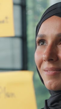 Satisfied islamic business woman analyzing stickers on glass in office Muslim businesswoman in hijab company CEO entrepreneur female girl reading sticky notes data plans smiling management work task